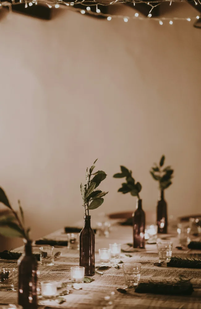 Table de dîner élégamment décorée avec bougies, bouteilles transformées en vases et feuillages, évoquant l’atmosphère chaleureuse des soirées organisées par Solal Events au Portugal.
